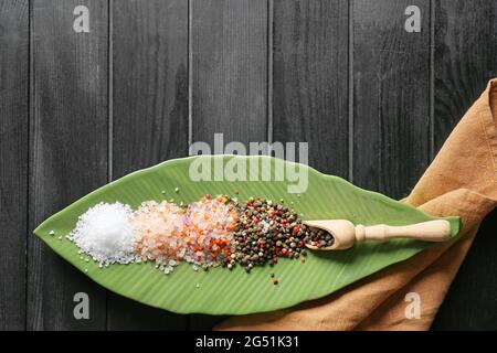 Teller mit verschiedenen Salz- und Pfefferkörnern auf dunklem Holzgrund Stockfoto