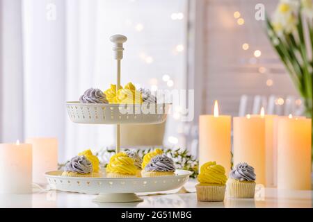 Dessertständer mit leckeren Cupcakes und brennenden Kerzen auf dem Tisch Stockfoto