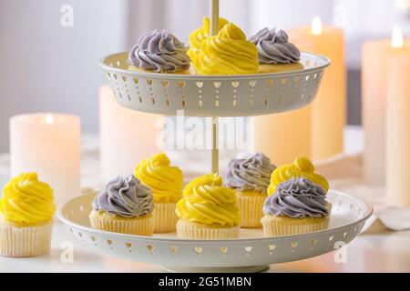 Dessertständer mit leckeren Cupcakes und brennenden Kerzen auf dem Tisch Stockfoto