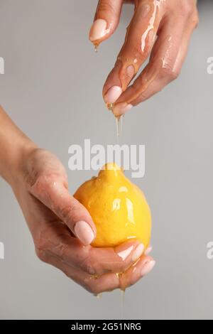 Weibliche Hände mit reifer Zitrone und tropfendem Honig auf grauem Hintergrund, Nahaufnahme Stockfoto