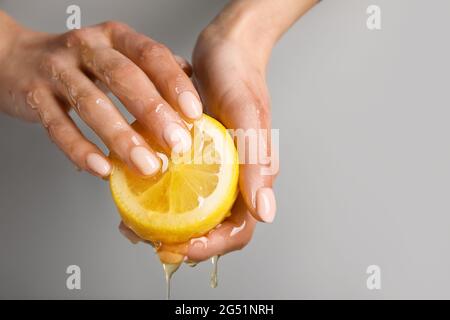 Weibliche Hände mit reifer Zitrone und tropfendem Honig auf grauem Hintergrund, Nahaufnahme Stockfoto