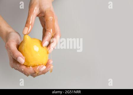 Weibliche Hände mit reifer Zitrone und tropfendem Honig auf grauem Hintergrund Stockfoto