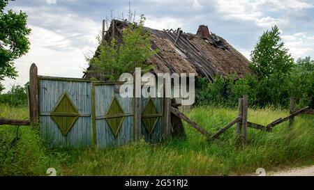 Altes verlassenes Haus mit Strohdach und altem Holztor Stockfoto