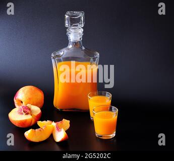 Zwei Gläser und eine Flasche Aprikosenlikör mit geschnittenen reifen Früchten auf schwarzem Hintergrund. Nahaufnahme. Stockfoto