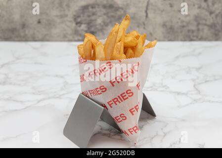 Beilage einer Tüte knuspriger pommes Frites, die in einer Tüte serviert und aufrecht präsentiert werden, um eine großartige Vorspeise zu genießen. Stockfoto