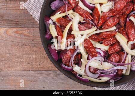 Gebratene Würstchen mit Gemüse in einer eisernen Pfanne. Ein Fleischgericht mit Paprika und Zwiebeln kochen Stockfoto