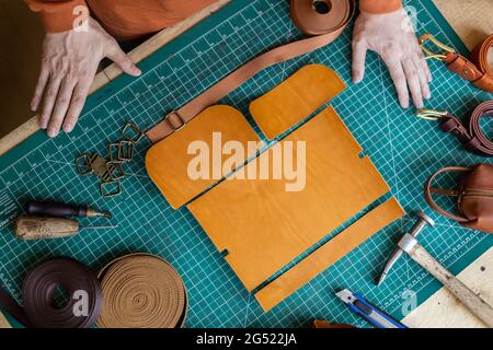 Prozess Schneidschema von Beutel mit Geräten und Materialien. Männlicher Gerber, der in der Lederwerkstatt arbeitet Stockfoto