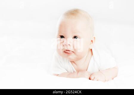 Der drei Monate alte kaukasische Junge liegt auf dem Bauch mit erhobenem Kopf und erhobener Zunge. Isoliert auf weißem Hintergrund. Stockfoto