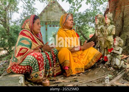Zwei reife Damen aus dem ländlichen Indien beten im Freien mit gefalteten Händen und tragen ethnischen Saree. Sie verehren Götzen der Götter der hinduistischen Mythologie. Stockfoto