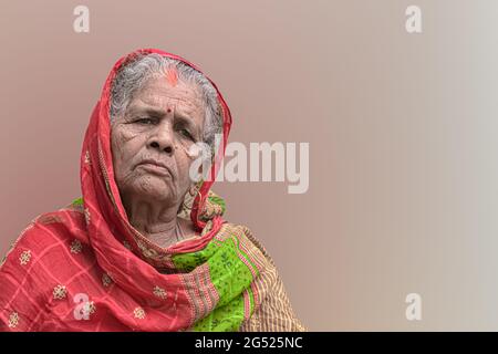 Schönes Porträt einer älteren Frau aus Indien, mit Falten im Gesicht und weiß grauen Haaren, tragen bunte ethnische rote Saree mit Schleier und nachdenklich. Stockfoto