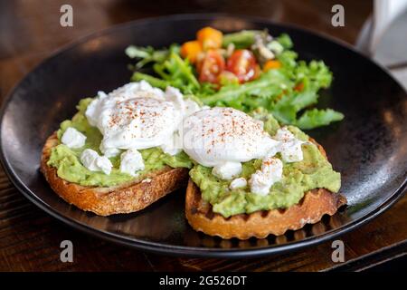 Zwei Avocado-Toasts mit pochierten Eiern und frischem Salat auf der Seite, gesundes, leckeres Frühstück Stockfoto