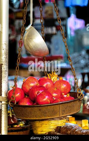 Granatäpfel in einer alten Metallwaage, die mit rostigen Ketten und einem Löffel darüber hing. Aufgenommen mit geringer Schärfentiefe. Stockfoto