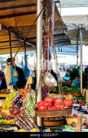 Granatäpfel in einer alten Metallwaage mit rostigen Ketten und trockenen Tomaten, Obst und Gemüse im Hintergrund. Stockfoto