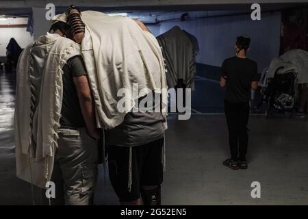 Jerusalem, Israel. 25. Juni 2021. Ein Vater segnet seine Söhne unter Gebetsschals, während jüdische Männer ihre Morgengebete in einer Tiefgarage in einem Akt selbstauferlegter sozialer Distanzierung durchführen, der im Moment nicht obligatorisch ist. 138 neue Fälle von COVID-19 wurden gestern festgestellt, mehr als fünfzig Prozent bei Jugendlichen unter 15 Jahren, die Mehrheit der Typ-Delta-Variante. PM Bennett kündigte an, dass die Regierung den Anstieg der Coronavirus-Fälle als neuen Ausbruch behandelt und Maßnahmen zur Bekämpfung der Krankheit ergreift. Ab heute 12 Uhr sind Gesichtsmasken wieder in Innenräumen Pflicht. Kredit: Nir Alon/Ala Stockfoto