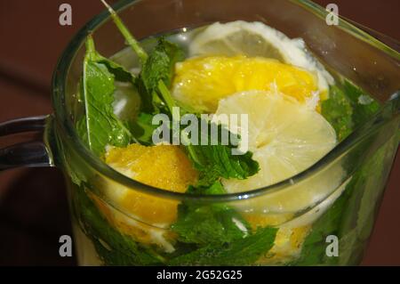 Ein kaltes Zitronengetränk in einem Glaskrug. Frische, frisch zubereitete Limonade. Bio-Minzgetränk mit Zitrusscheiben. Stockfoto