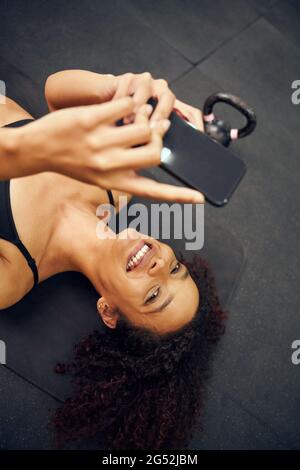 Afroamerikanische Frau, die auf dem Boden liegt und ein Foto gemacht hat. Schöne Mischling Frau lächelnd während der Aufnahme des Fotos. Hochwertige Fotos Stockfoto