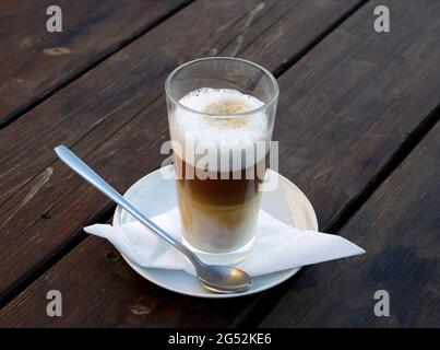 Caffe Latte Macchiato, ein Glas Kaffee mit aufgeschäumter Milch auf einem hölzernen Hintergrund. Seine Kaffeezeit. Stockfoto