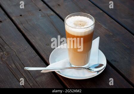 Caffe Latte Macchiato, ein Glas Kaffee mit aufgeschäumter Milch auf einem hölzernen Hintergrund. Seine Kaffeezeit. Stockfoto
