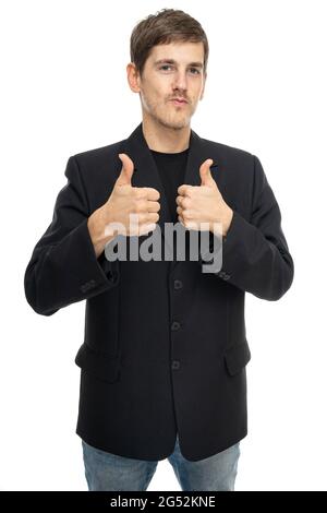 Der junge, hübsche, große, schlanke weiße Mann mit braunen Haaren zeigt den Daumen in schwarzem Blazer in blauer Jeans, isoliert auf weißem Hintergrund Stockfoto