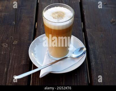 Caffe Latte Macchiato, ein Glas Kaffee mit aufgeschäumter Milch auf einem hölzernen Hintergrund. Seine Kaffeezeit. Stockfoto