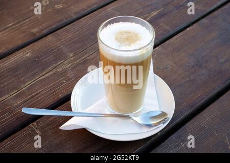 Caffe Latte Macchiato, ein Glas Kaffee mit aufgeschäumter Milch auf einem hölzernen Hintergrund. Seine Kaffeezeit. Stockfoto