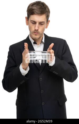 Junger, hübscher, großer, schlanker weißer Mann mit braunem Haar, der ein Glas Wasser horizontal in einem schwarzen Blazer hält, der auf weißem Hintergrund isoliert ist Stockfoto
