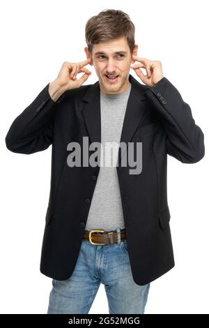 Der junge, hübsche, große, schlanke weiße Mann mit braunen Haaren bedeckt seine Ohren mit einem schwarzen Blazer in einem grauen Hemd, das auf weißem Hintergrund isoliert ist Stockfoto