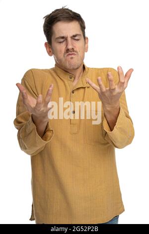 Junger, hübscher, großer, schlanker weißer Mann mit braunem Haar sieht wütend in ockerfarbenem Hemd aus, das auf weißem Hintergrund isoliert ist Stockfoto
