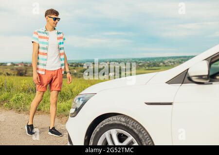 Glücklicher junger Mann in Sonnenbrille, junger Mann lächelt und reist an einem sonnigen Tag mit dem Auto im Freien Stockfoto