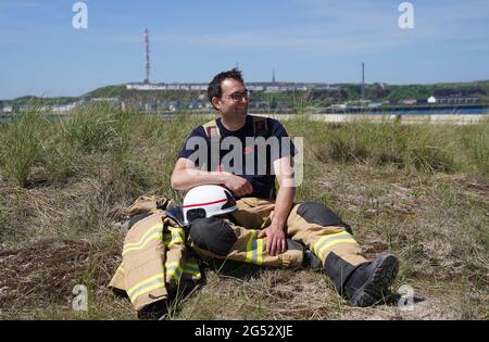 16. Juni 2021, Schleswig-Holstein, Helgoland: Felix Vorndran von der Freiwilligen Feuerwehr Bergisch-Gladbach sitzt während seines Dünendienstes auf der Düne der Hochseeinsel Helgoland an der Feuerwache. Feuerwehrleute aus ganz Deutschland können auf der Hochseeinsel Helgoland das angenehme mit dem Nützlichen während der Saison verbinden. Die Gemeinde sucht nach der Sicherung des Brandschutzes auf der Düne freiwillige Feuerwehrkameraden und -Genossen, die mit Ihrem Einsatz die touristische Nutzung der Düne aufrechterhalten. Die Feuerwehrmänner vom Festland sind in Bungalows auf untergebracht Stockfoto