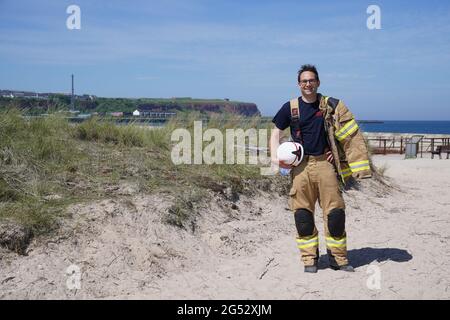 16. Juni 2021, Schleswig-Holstein, Helgoland: Felix Vorndran von der Freiwilligen Feuerwehr Bergisch-Gladbach steht während seines Dünendienstes auf der Düne der Tiefseeinsel Helgoland an der Feuerwache. Feuerwehrleute aus ganz Deutschland können auf der Hochseeinsel Helgoland das angenehme mit dem Nützlichen während der Saison verbinden. Die Gemeinde sucht nach der Sicherung des Brandschutzes auf der Düne freiwillige Feuerwehrkameraden und -Genossen, die mit Ihrem Einsatz die touristische Nutzung der Düne aufrechterhalten. Die Feuerwehrmänner vom Festland sind in Bungalows auf untergebracht Stockfoto