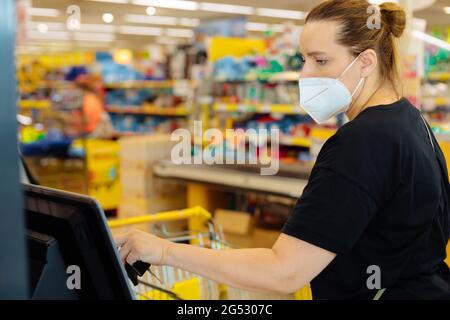 Frau in einem Supermarkt an einem Selbstbedienungsschalter einkaufen in einer medizinischen Maske, Covid Sicherheit, Stadtleben Stockfoto