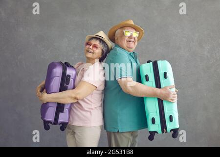 Studioportrait von glücklichen älteren Touristen, die Rücken an Rücken stehen und Koffer halten Stockfoto