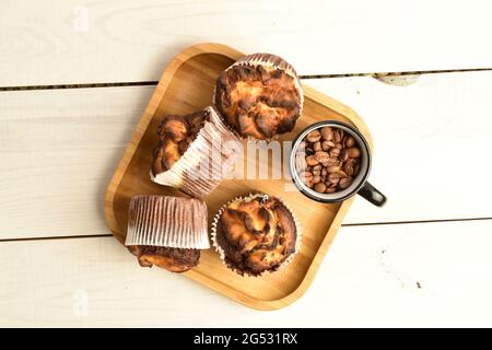 Vier duftende Schokoladenkuckuffins mit einer Tasse auf einem Bambustablett, Nahaufnahme, auf einem weißen Holztisch, Draufsicht. Stockfoto