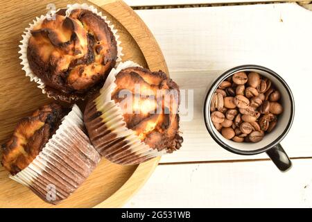 Drei duftende Schokoladenkuckuffins auf einem runden Holztablett mit einer Tasse Kaffee, Nahaufnahme, auf einem weißen Holztisch, Draufsicht. Stockfoto