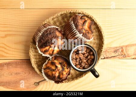 Drei duftende Schokoladenkuhmuffins mit einer Tasse Kaffee auf einem Strohhalmtablett, Nahaufnahme, auf einem Holztisch, Draufsicht. Stockfoto