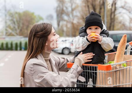 Baby Junge im Warenkorb hält frische Orange in der Nähe glückliche Mutter Stockfoto