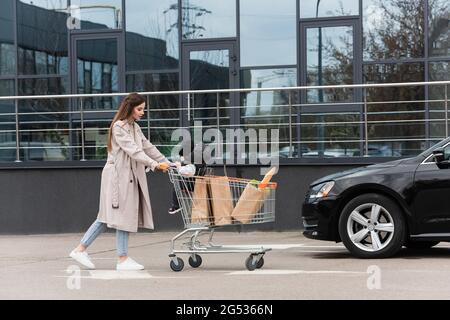 Junge Frau mit Sohn und Käufe im Warenkorb zu Fuß in Richtung Auto Stockfoto