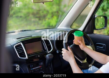 Eine gesichtslose Frau trinkt während der Fahrt Kaffee in einem Glas. Nehmen Sie ein heißes Tonic-Getränk zum Mitnehmen Stockfoto