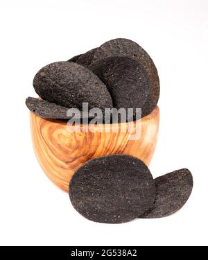 Schwarze Kartoffelchips in einer Olivenschale, isoliert auf weißem Hintergrund. Schwarze Chips mit Aktivkohle und rotem Pfeffer. Stockfoto