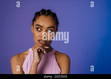 Nachdenkliche junge afrikanische Frau, die über blauem Wandhintergrund steht und wegschaut Stockfoto
