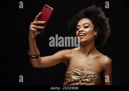 Glückliche afrikanische junge Frau im Kleid, die ein Selfie mit dem Handy im Studio macht Stockfoto
