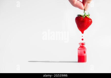 Die Hand hält Erdbeeren, mit denen die rote Saftflüssigkeit in eine Flasche abfließt Stockfoto