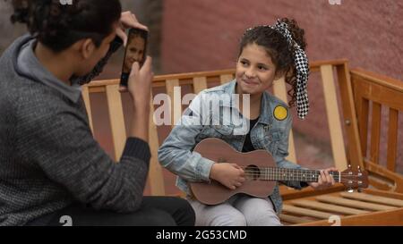 Junger hispanischer Mann lehrt lockiges Mädchen, Ukulele im Freien Musikkonzept zu spielen Stockfoto