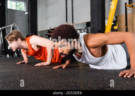 Bärtiger afroamerikanischer Mann, der Liegestütze in der Nähe von verschwommenem Sportler macht Stockfoto