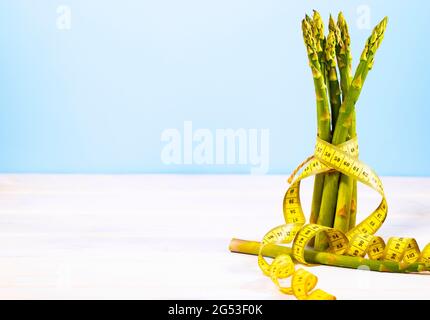 Bund frischer Spargel auf blauem Hintergrund mit Maßband. Ketogene Ernährung mit Vitaminen und Zellulose. Grünes Gemüse. Speicherplatz kopieren. Sauber Stockfoto