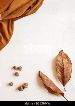 Rahmen aus braunem Pullover, Herbstblatt und Eicheln auf weißem Hintergrund. Draufsicht. Kopierbereich. Minimale Herbstzusammensetzung Stockfoto