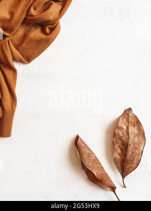 Rahmen aus braunem Pullover und Herbstblättern auf weißem Hintergrund. Draufsicht. Kopierbereich. Minimale Herbstzusammensetzung Stockfoto