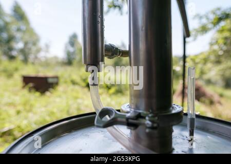 Alkoholmashine in einem Dorfhof, auf einem verschwommenen Hintergrund. Zubereitung eines berauschenden Getränks. Nahaufnahme. Stockfoto