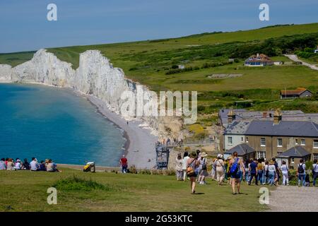 Staycation Idee. Touristen gehen den Hügel hinunter und sitzen auf dem Gras und schauen auf die weißen Kreidefelsen der Seven Sisters in Birling Gap, Großbritannien. Stockfoto